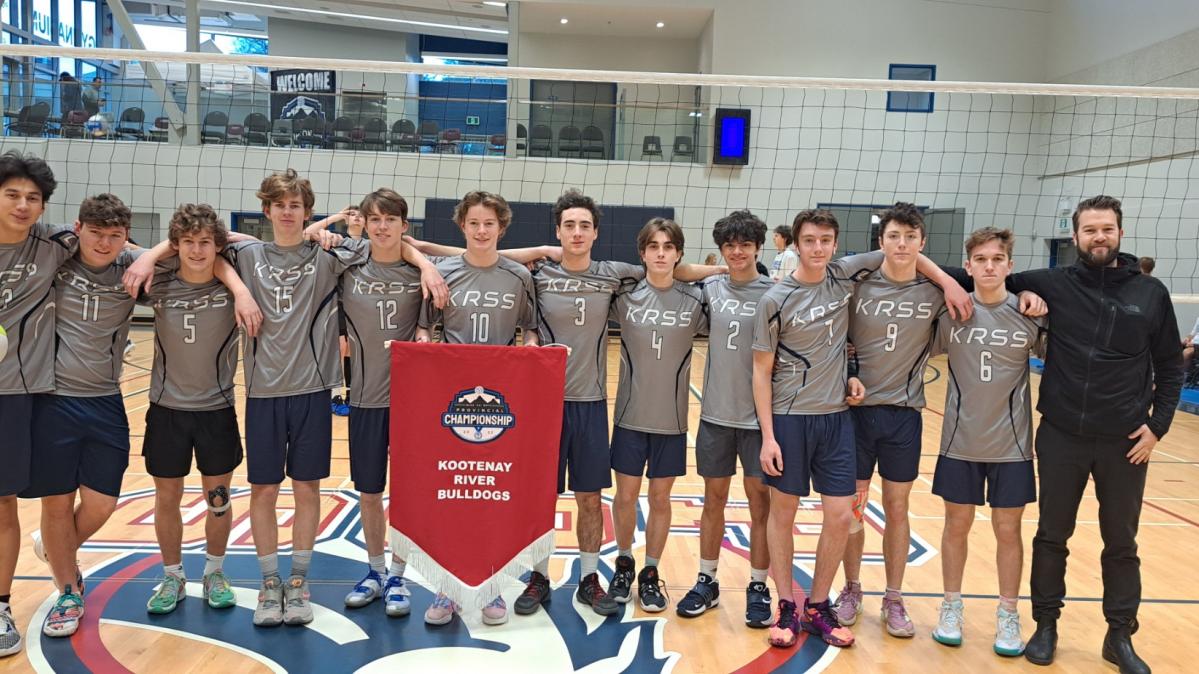 Senior boys' highschool volleyball team in grey shirts and black shorts with coach at right hand side and red team banner in front