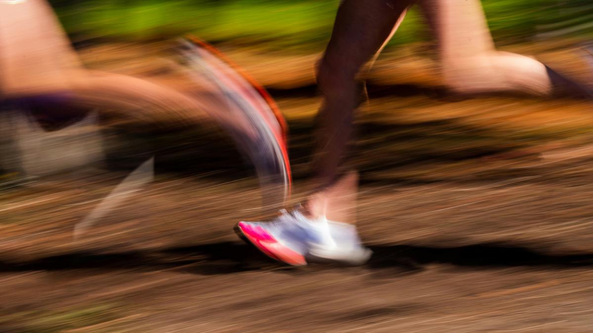 Blurry photo of two runners on a dirt track showing their bare legs and running shoes only