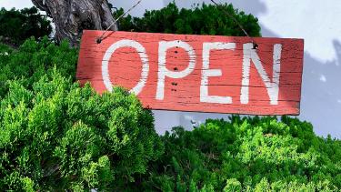 Green shrubs and mountainside behind red wooden sign that says, "open"