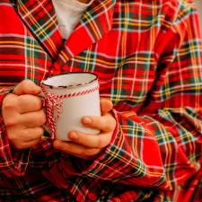 Person in red plaid pyjamas holding a white mug with a red and while striped string tied around it.